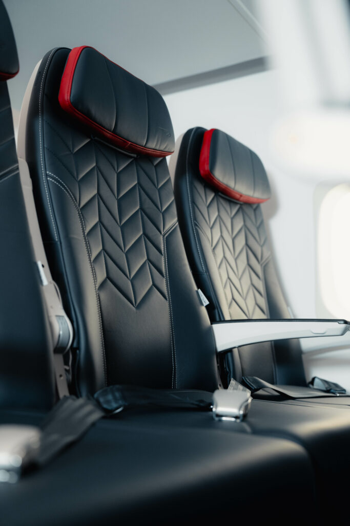 A close up of the Collins Meridian seat choosen by British Airways (BA) shows an arrow like pattern and red detailing around the headrest. The armrest is situated up on one seat to show it's flexibility.