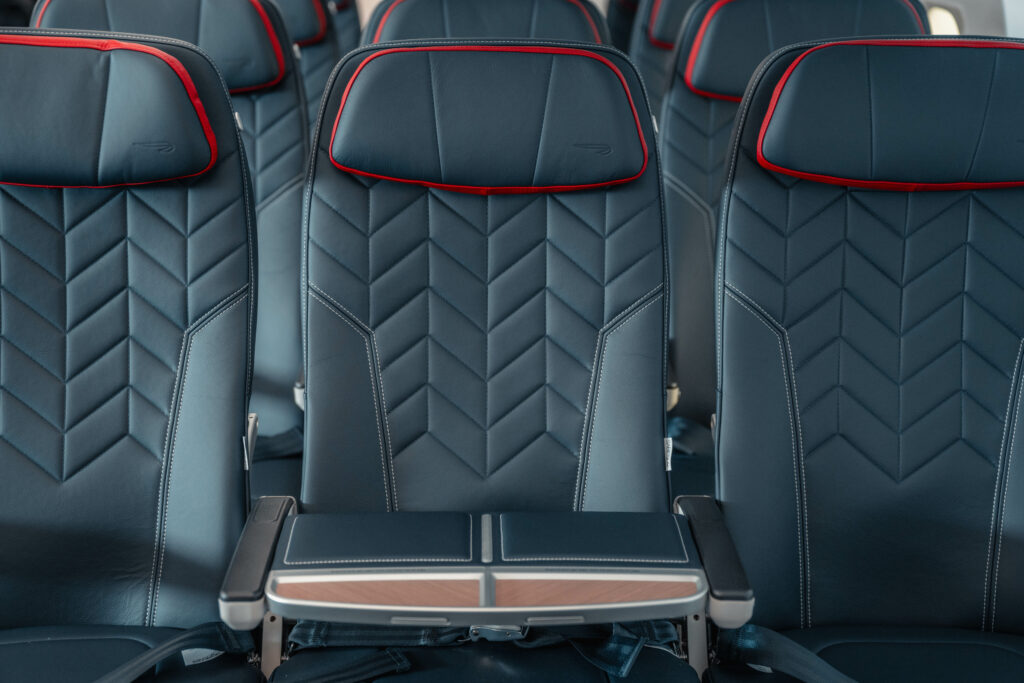 A close up of the Collins Meridian seat choosen by British Airways (BA) shows an arrow like pattern and red detailing around the headrest. A tray is situated in the middle seat to block it off from passengers.