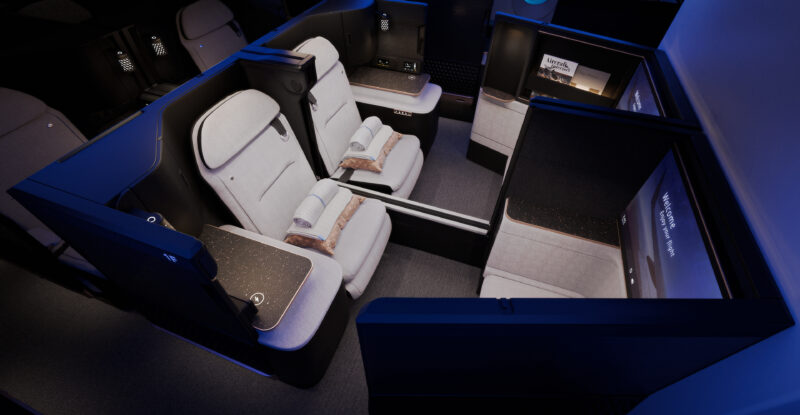 A rendering of the Safran Unity Elite business class seat. The all white seat gives a luxurious feel with black trim and blue LED Lighting. Two seats with the middle privacy door down.