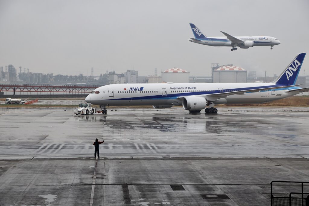 ANA 787-10 arrives at the airport . An in-air ANA jet is seen behind it.