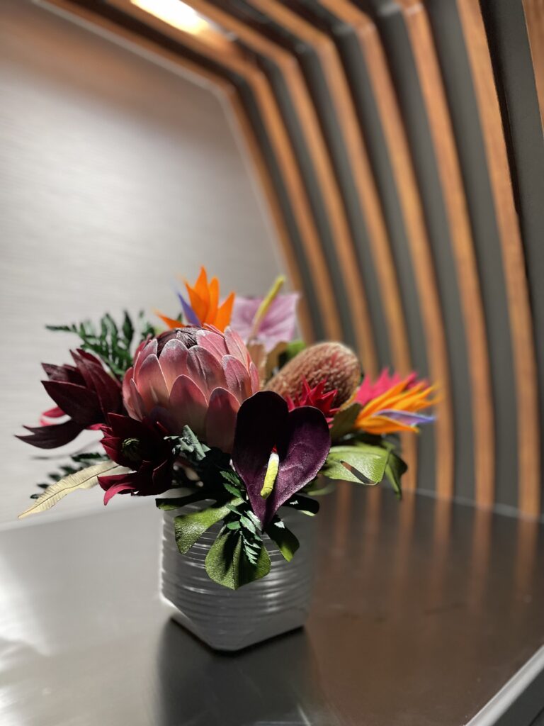 A floral arrangement sits at the entrance of the Hawaiian Airlines 787-9 Dreamliner. ribbed wood paneling arch the entry way.