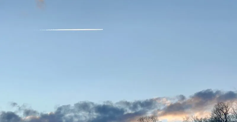Aircraft flying high overhead, above a hill with trees