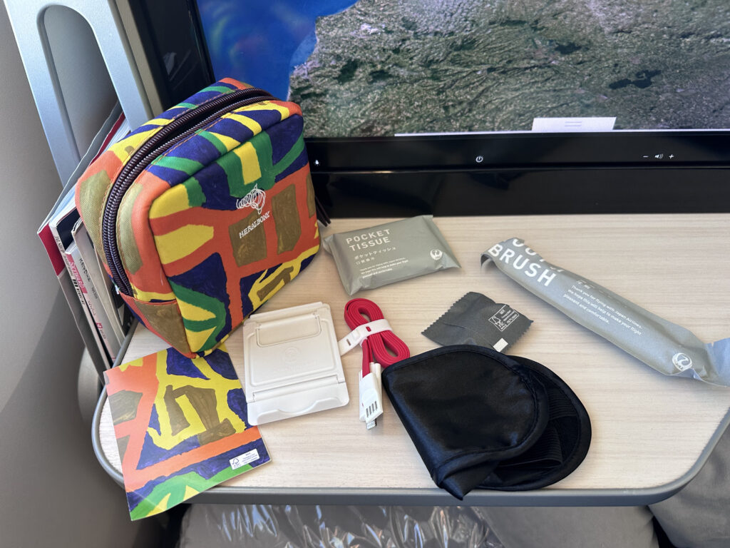 A colorful business class amenity kit and its contents are set out on the tray table.