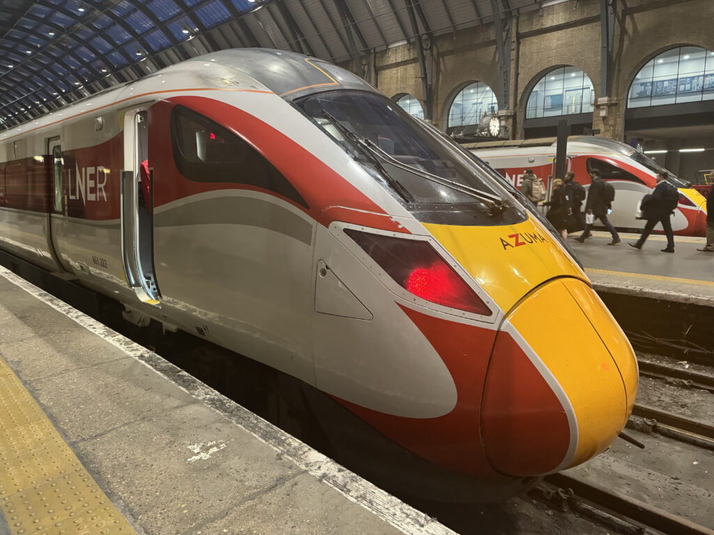 The nose of the LNER rail car as it arrives at the platform.The livery is red, yellow, grey and white.