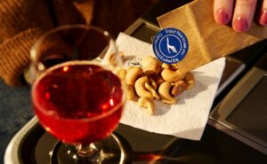 A Lufthansa passenger is pouring welcome nuts onto a napkin laid out next to a drink.