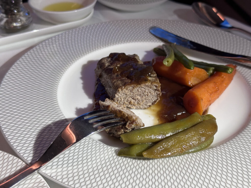 A piece of meat in a sauce with beans and carrots as a side. The meat is cut to show its texture.