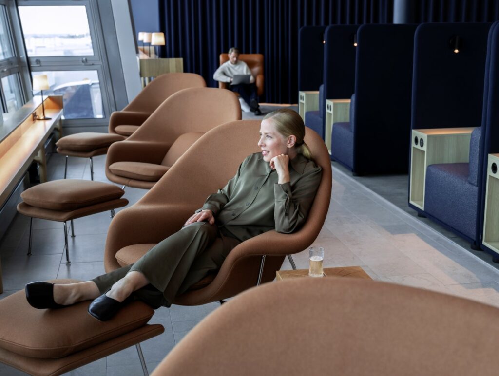 A women is sitting in a large brown chair, legs on an ottoman, looking out the window in the Finnair Lounge