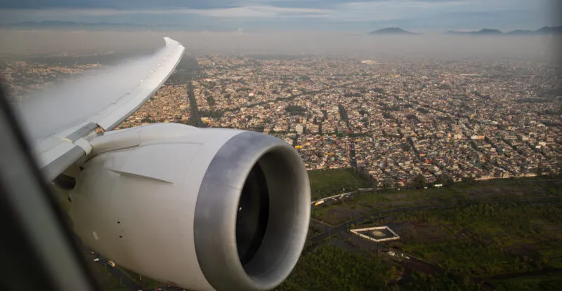Looking out the AeroMexico aircraft over a city. The wing and engine are in view.