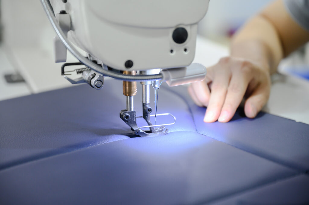 A Muirhead employee uses a sewing machine to stitch a blue seat cover.