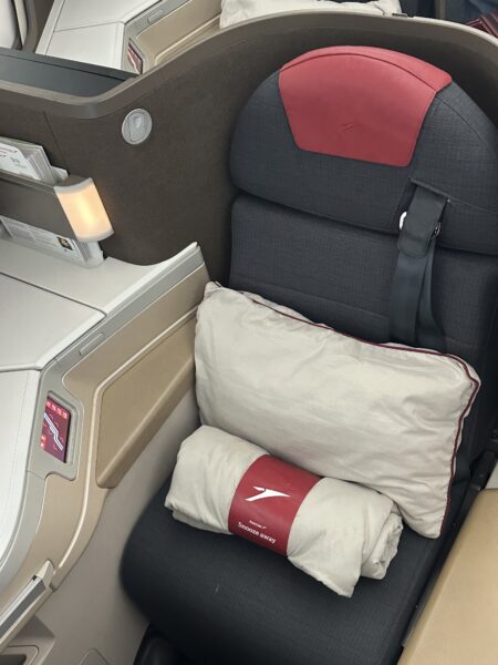Close up of Austrian Airlines business class seat with bedding sitting atop it, and splashes of red in the soft product.