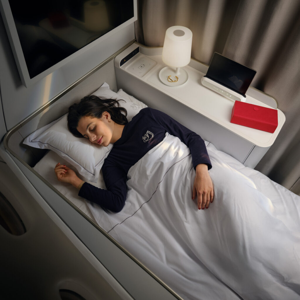 An overhead view of the woman passenger asleep in her first class bed aboard an Air France 777. The side table features a wireless charger.