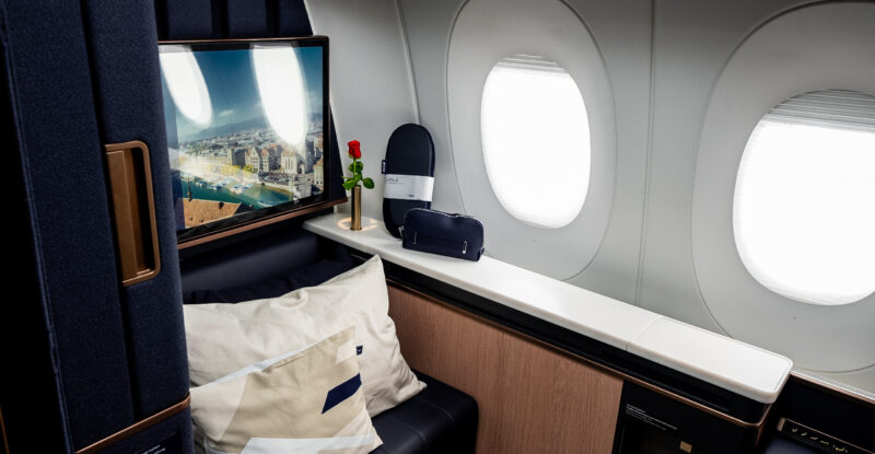 Lufthansa first class window with a white blanket on top of a large dark blue seat