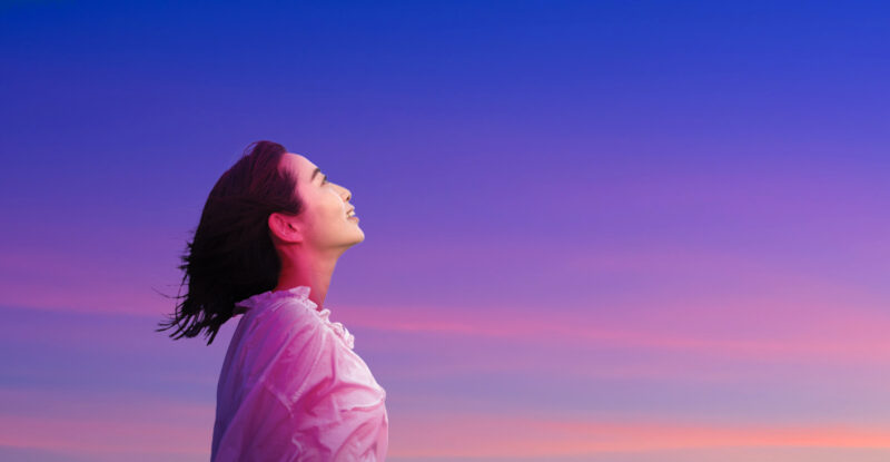 A woman is looking up as the sun rises.