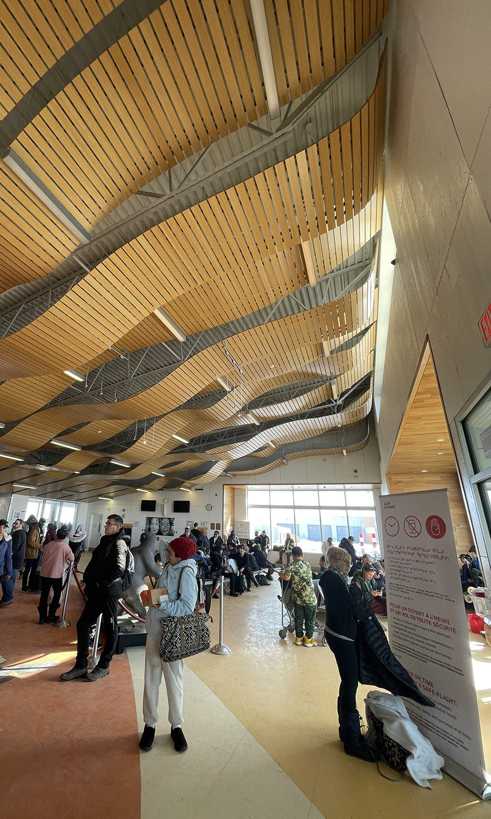 Puvirnituq airport terminal features sweeping design of wood slats. Passengers prepare to board.