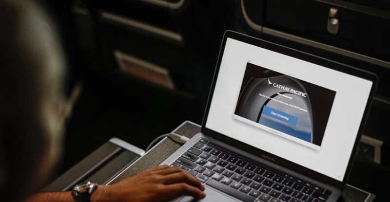 Cathay Pacific passenger is searching the carrier's website on a laptop while also watching content on the seatback IFE