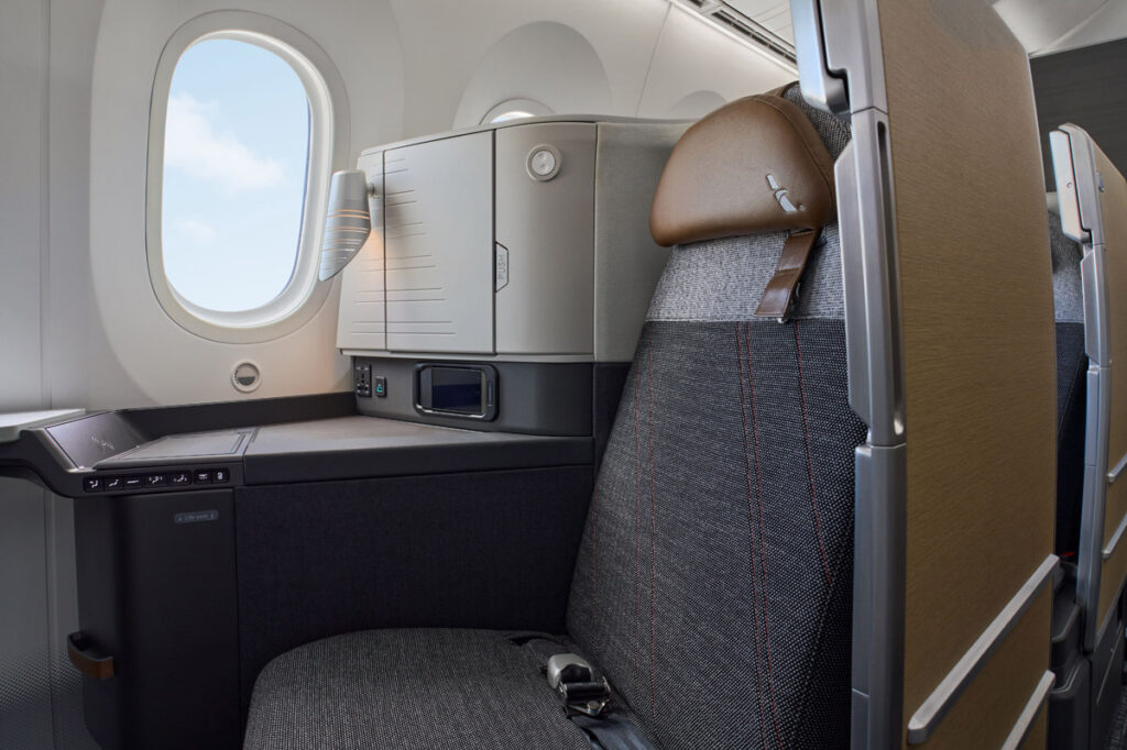 Customers in Flagship Suite® seats are surrounded with comfort with more personal space and a one-of-a-kind chaise lounge option. This photograph of a window seat shows the muted greys, browns, and beige palette. 