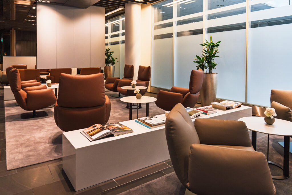 The Lufthansa First Class Lounge in Terminal 2 at Munich Airport features a variety of seating options including brown armchairs beside small white tables