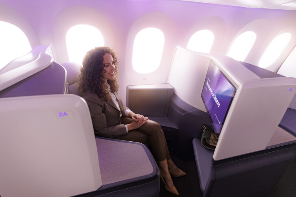 A woman sits in a window-seat Business Premier suite. Purple LEDs cast a pretty glow.