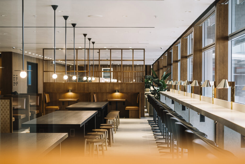 A long table with stools at the window, as well as booths and regular dining tables.