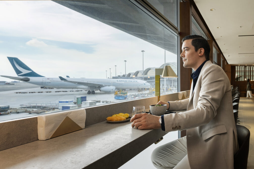 A man is sitting at the large windows in The Bridge looking out at the runway and gates