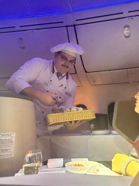 Flying chef distributes bread rolls to passengers on this Austrian 787 flight.