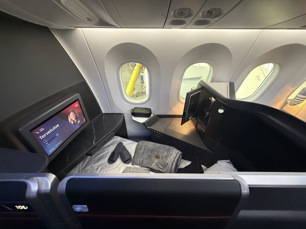Overhead view of Flagship Suite Preferred window seat in bed mode, with bedding and soft product laid out. 