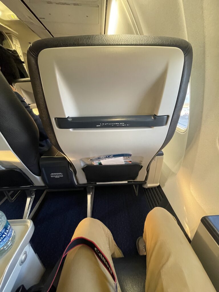 The author's legs have plenty of legroom in this Premium seat. The seatback in front of him is in view, including a lower literature pocket.