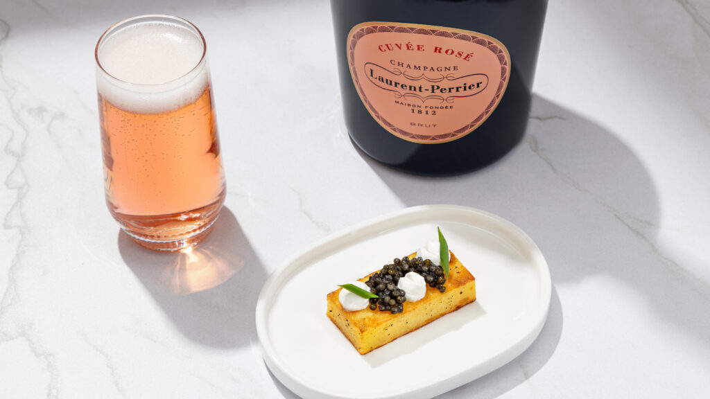 A glass of champagne and caviar sit on a white surface.