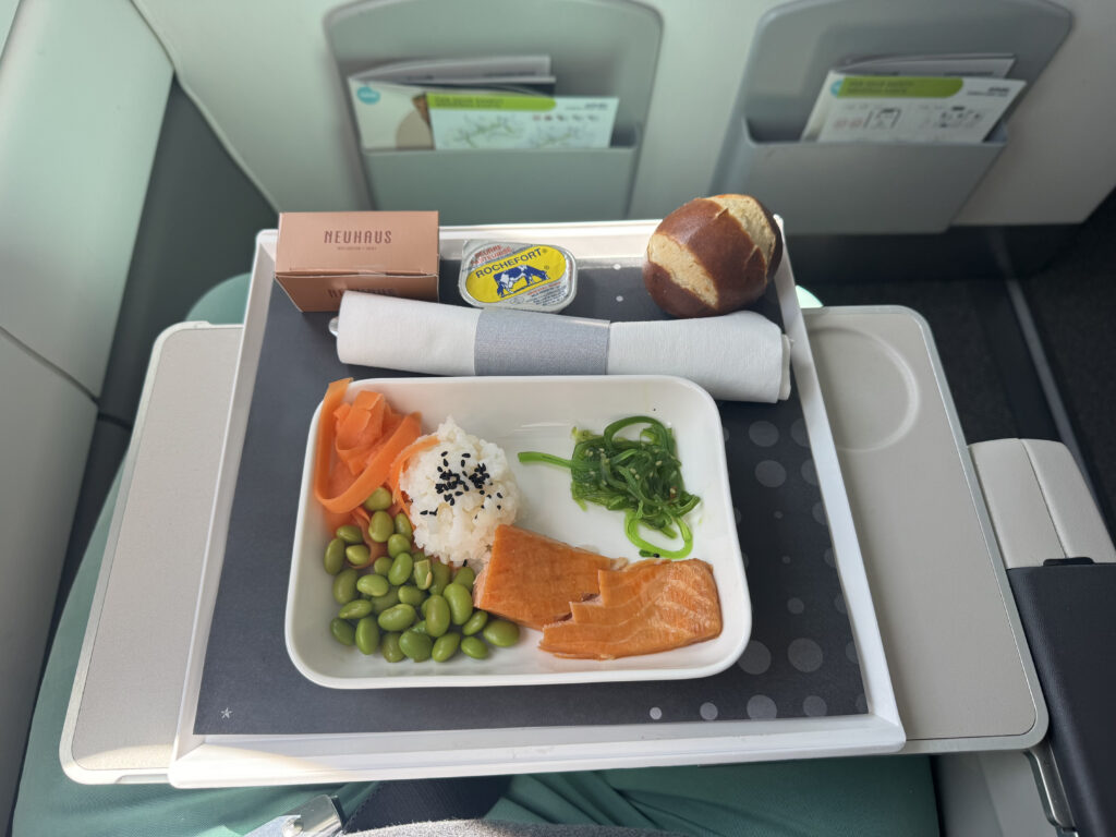 An inflight meal, featuring salmon and sides, is displayed on the aircraft tray table for Brussels Airlines
