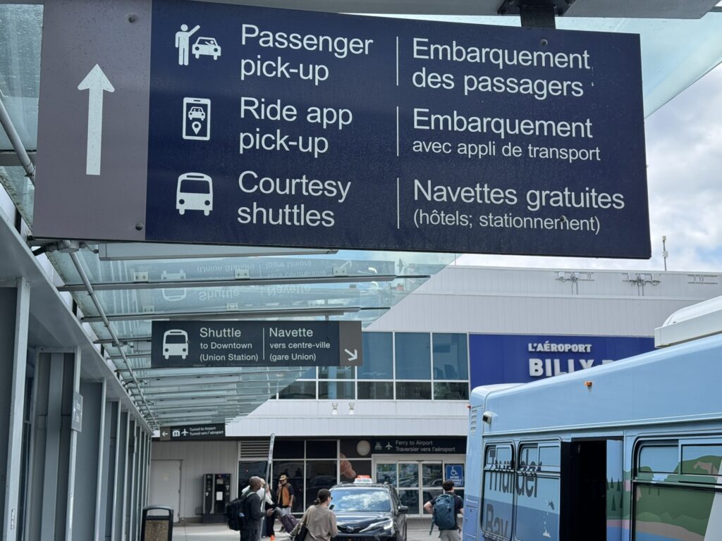 An airport sign with directions for passenger pick-up, ride app pick-up, and courtesy shuttles. 