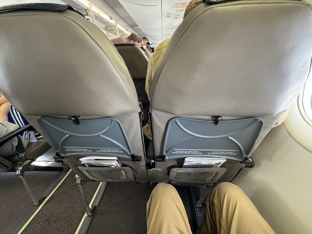 A man's knees are seen fairly close to the seat in front of him on this Porter flight. The seats are dark beige and appear bare bones.