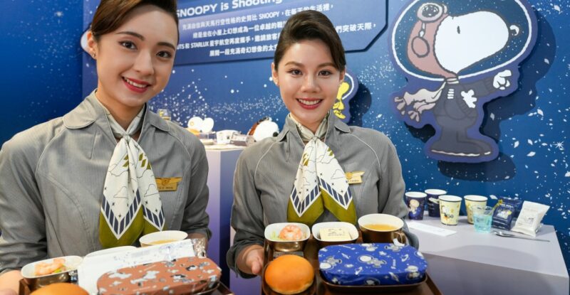 Two STARLUX flight crew members hold PEANUTS themed meals