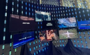 Lots of large IFE displays hang on a wall, showcasing different channels, including in the bottom left, a screen that stays "Starlink/United" to represent the integration of IFC and IFE.