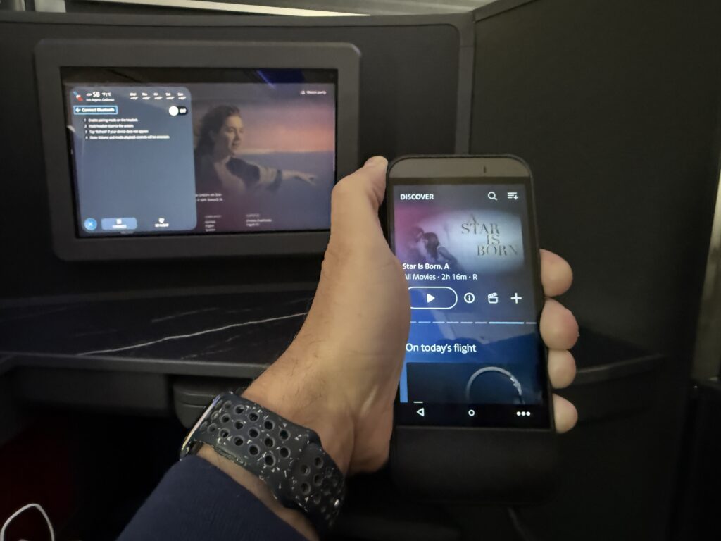 The embedded IFE screen is in the background and the IFE remote is being held by the author in the foreground.