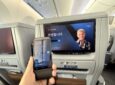 The passenger holds up the tethered IFE remote to the IFE screen in Premium Economy class.