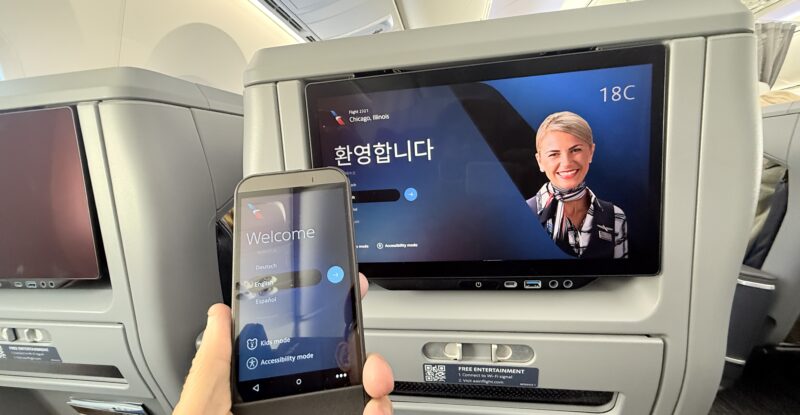 The passenger holds up the tethered IFE remote to the IFE screen in Premium Economy class.