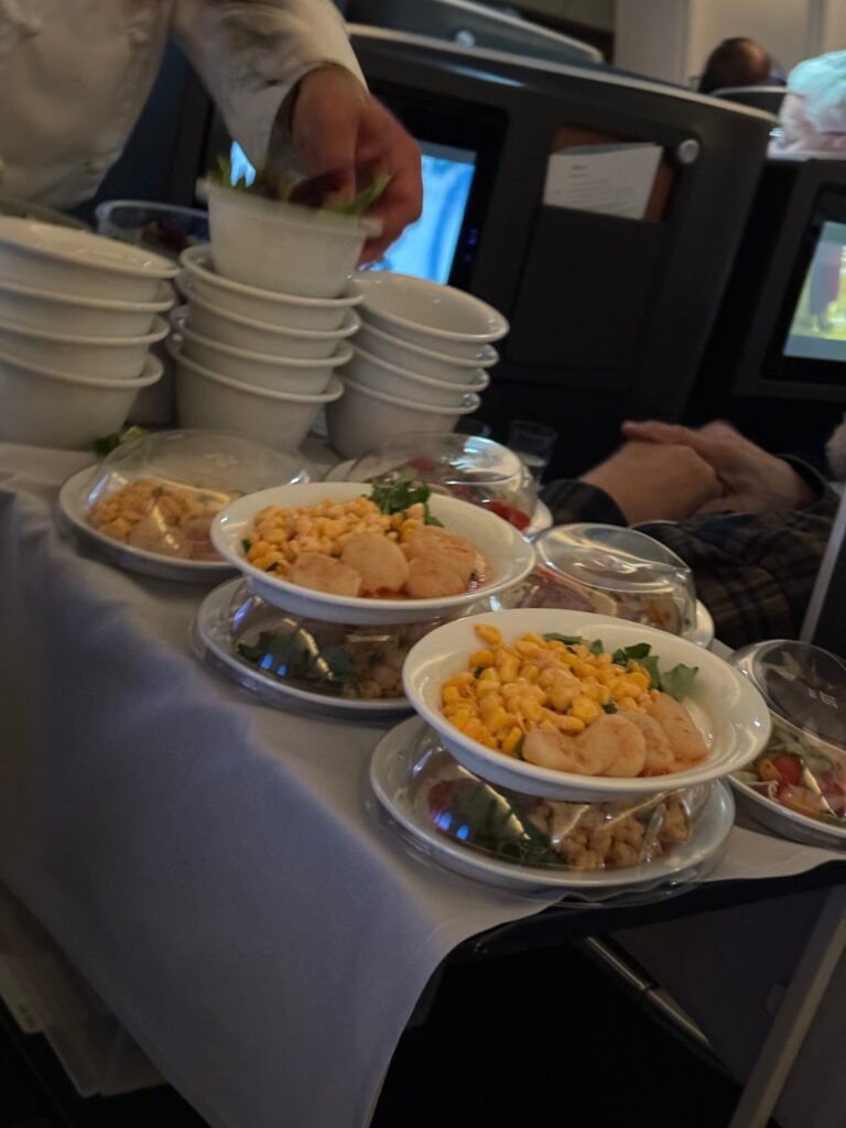 Plates of food are on the galley cart. A crew member distributes the various dishes to passengers.