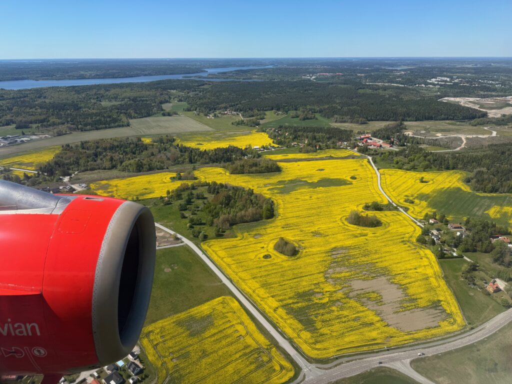 Red painted engine as seen through the window, as the aircraft flies over green and yellow fields.