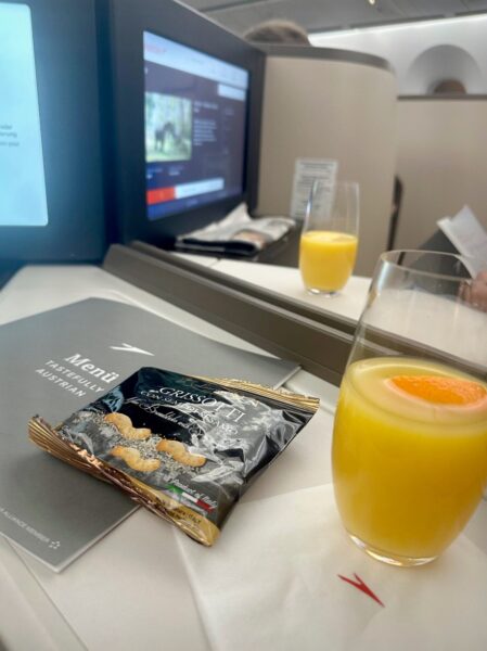 Divider is down between a center pair in Austrian business class. Juice and nuts sit atop the side tables of each suite.