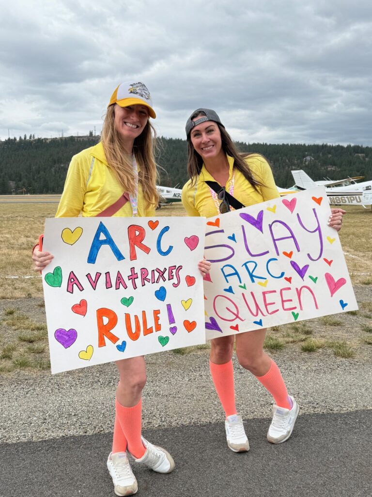 The Felts Field Sky Queens — Team 1 — welcoming other teams at the end of the race. Two women are holding signs celebrating the teams. Image: Harriet Baskas