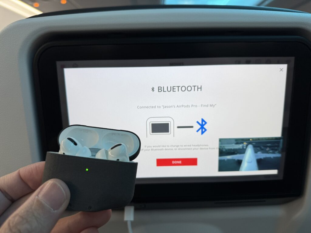 The author holds a pair of AirPods up to the IFE screen to connect via Bluetooth.
