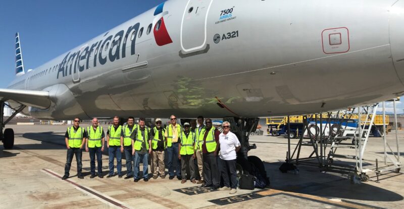 A group of technicians are standing for a photo in front of an American Airlines aircraft.