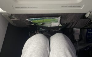 A woman's knees are seen a a short distance from the seat in front of her in economy class on an Aer Lingus flight