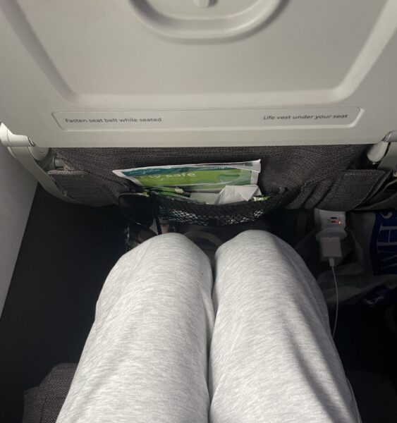 A woman's knees are seen a a short distance from the seat in front of her in economy class on an Aer Lingus flight