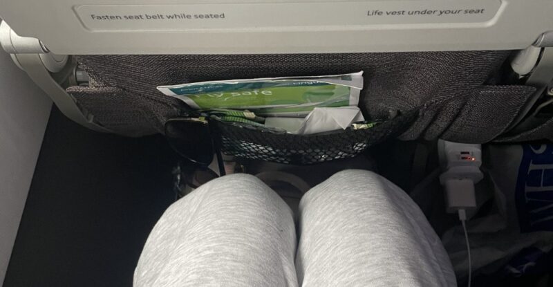 A woman's knees are seen a a short distance from the seat in front of her in economy class on an Aer Lingus flight