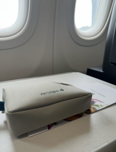 Aer Lingus cream color amenity kits sits on the aircraft tray table in front of the window as the sun shines in. 
