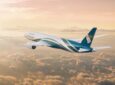 Oman Air Aircraft in flight at sunrise above scattered clouds.