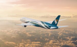 Oman Air Aircraft in flight at sunrise above scattered clouds.