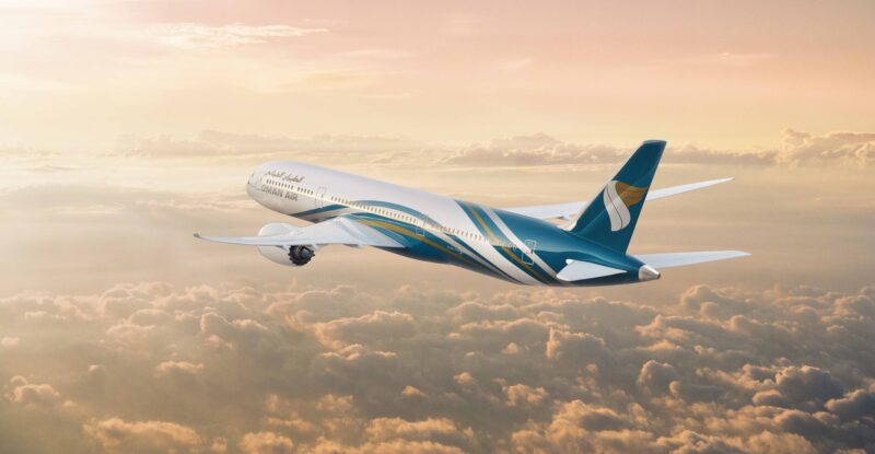 Oman Air Aircraft in flight at sunrise above scattered clouds.
