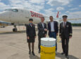 SWISS crew standing in front of an aircraft and a Synhelion barrel.